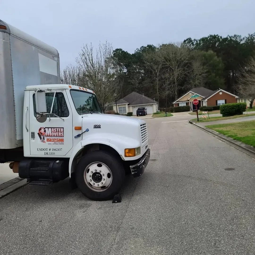 Master Movers of Tallahassee moving truck on a residential street near brick houses and trees.