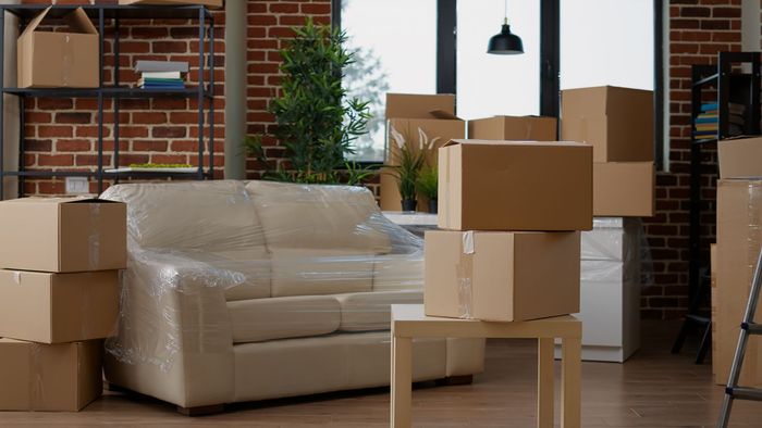 Boxes stacked around a wrapped sofa in a room, indicating a move.