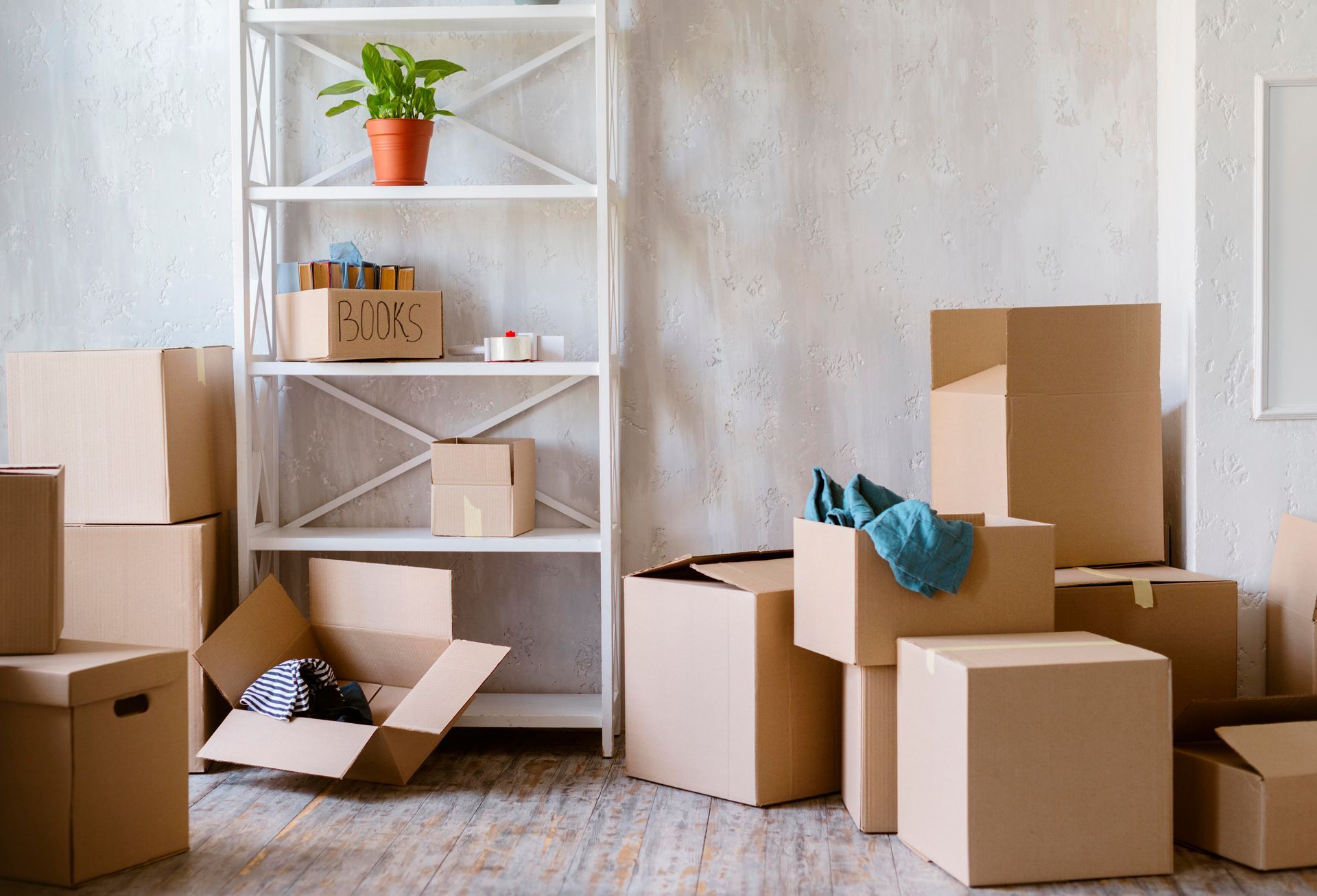 Boxes stacked near a white shelf with items, moving day.