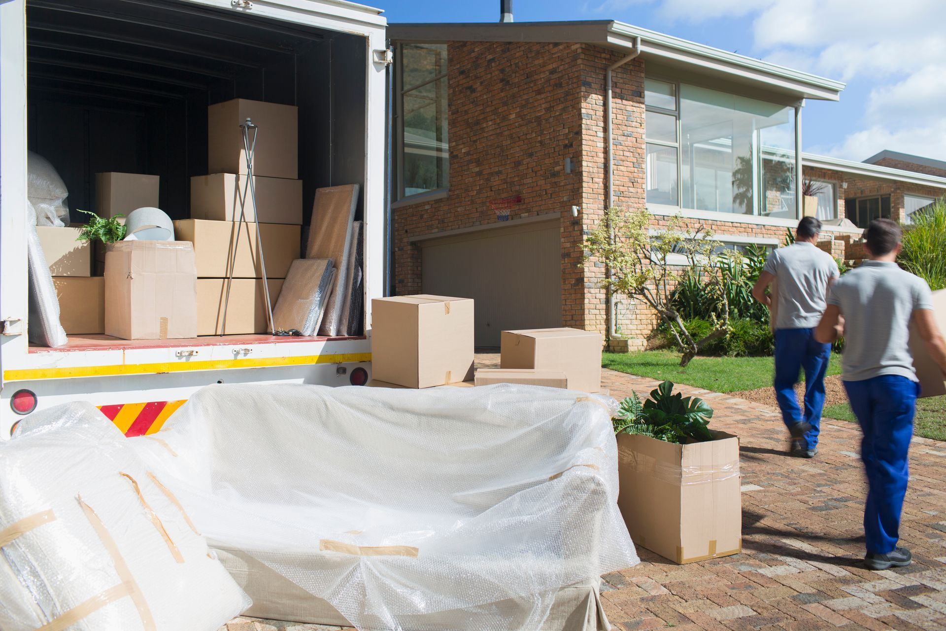 Movers loading boxes and furniture into a truck outside a house.