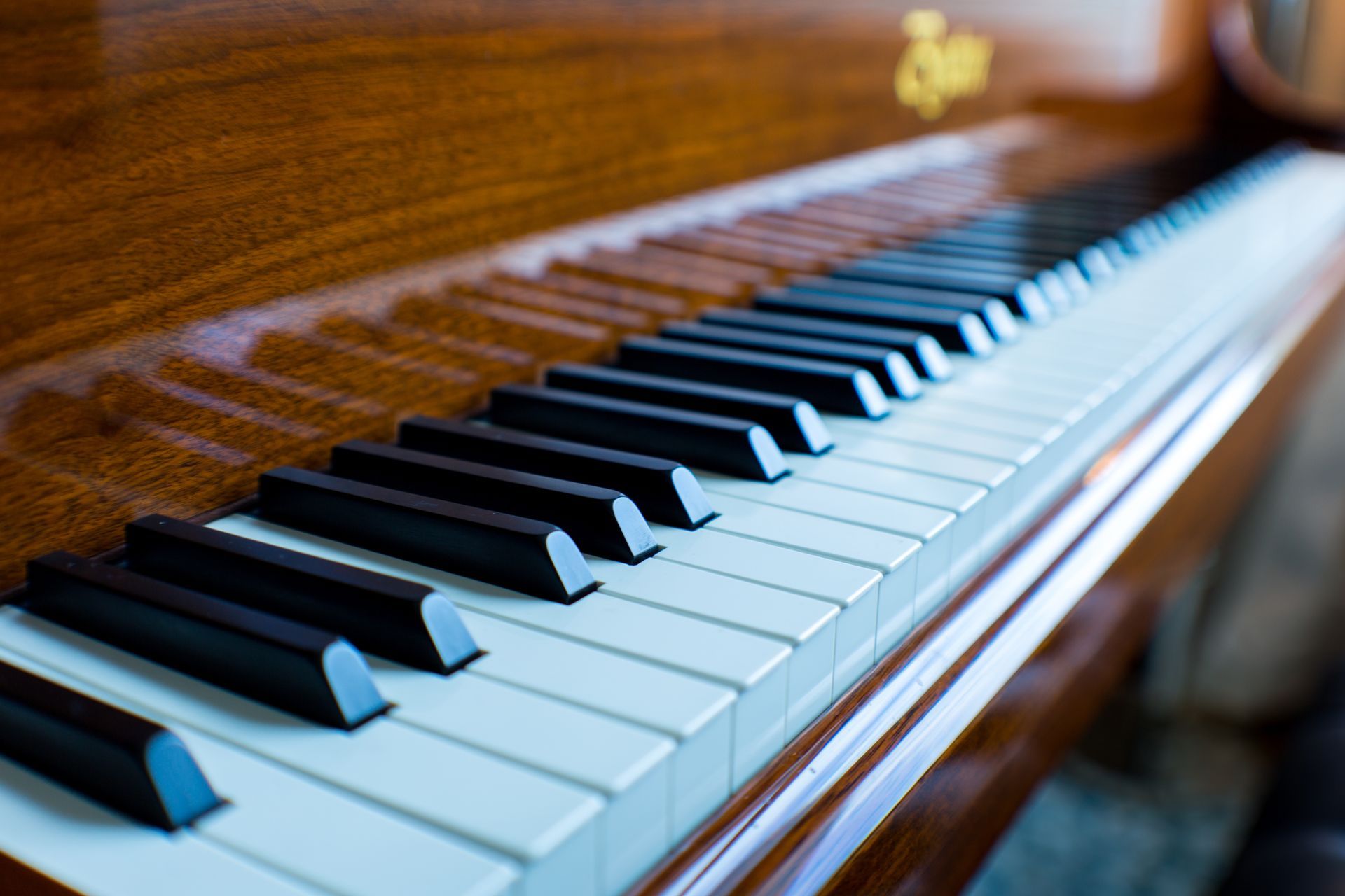 Piano keyboard with black and white keys, set in a wooden frame, and a golden logo.