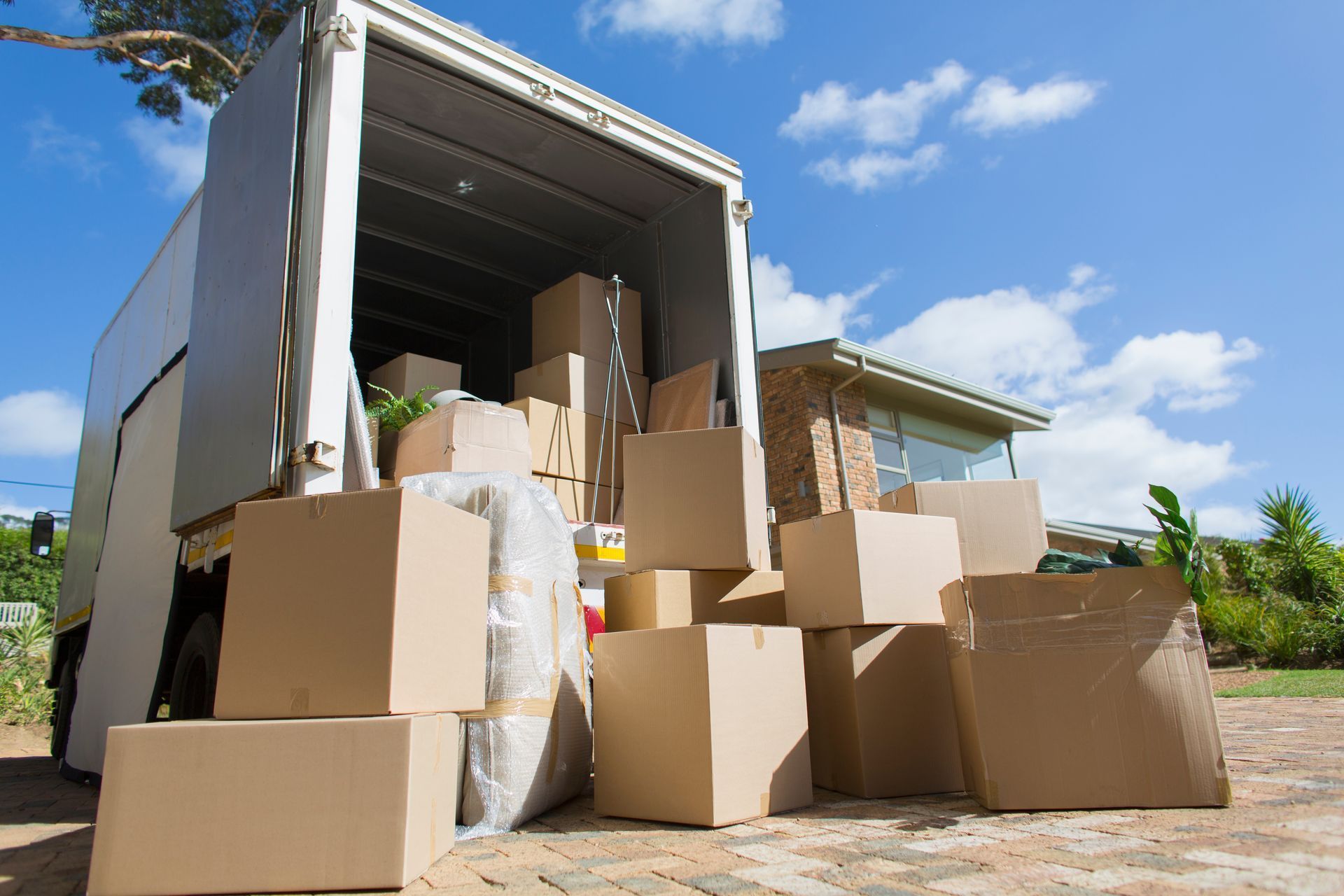 Boxes loaded in a moving truck, parked outside a house, on a sunny day.
