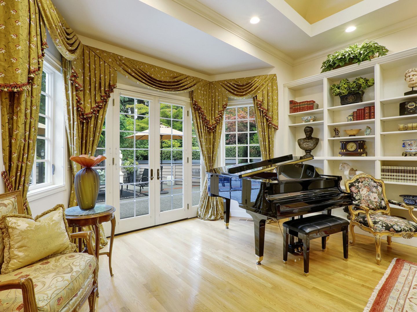 Elegant room with grand piano, French doors, ornate gold drapes, and built-in bookshelves.